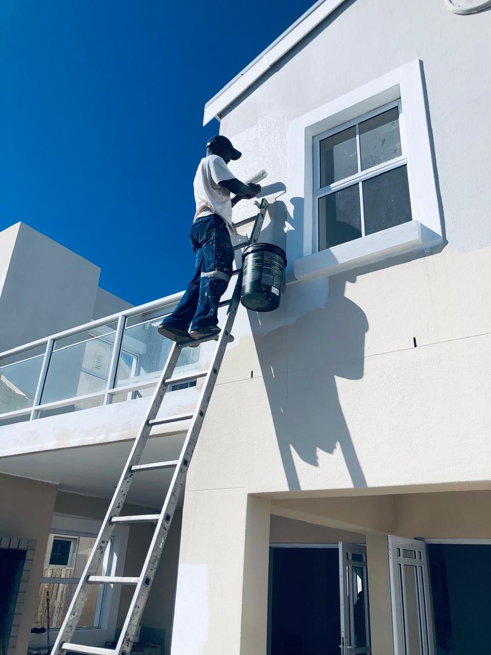 Painter up an extension ladder rolling the upper gable of a double-storey home