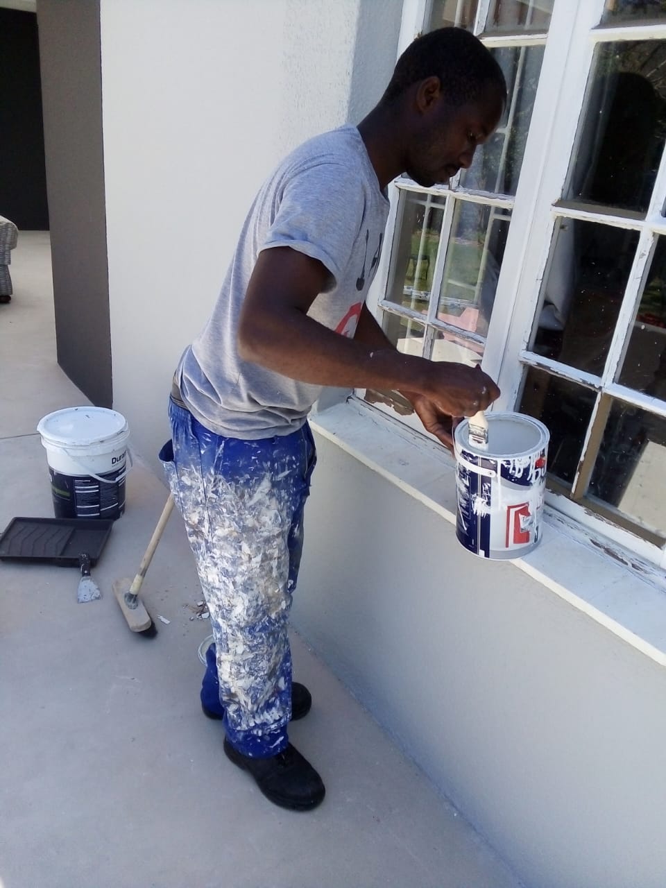 Painter loading a brush from a tin to hand-paint timber window frames white