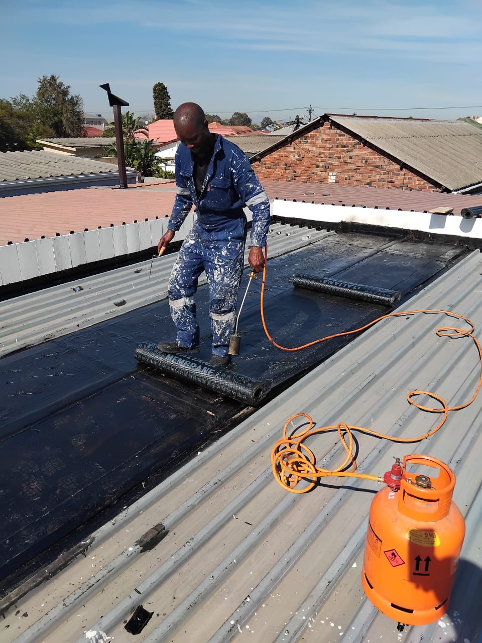 Torch-on bituminous membrane being laid along a metal roof box gutter with a gas torch
