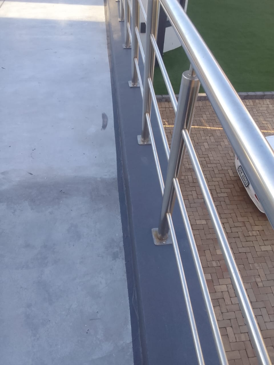 A balcony slab edge and upstand sealed with grey waterproof membrane against a stainless balustrade