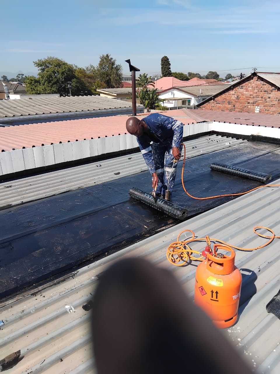 Torch-on membrane sheet being rolled out and heated on a metal roof